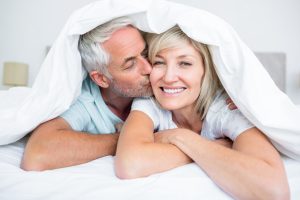 couple under comforter at home with man kissing woman