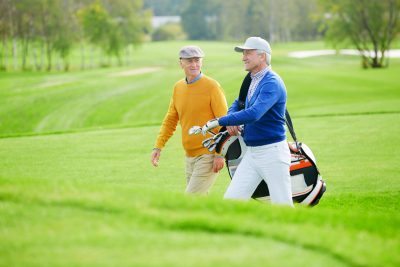 Two senior men walking with golf gear on golf ground.
